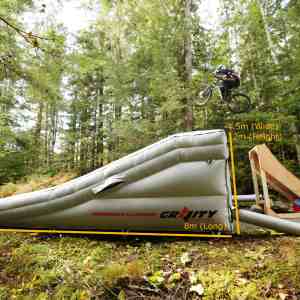 A mountain biker jumping off a Gravity Stunts built ramp about to land on the Mercury Lander which also shows dimensions of 8m long, 4.5m wide and 2m height