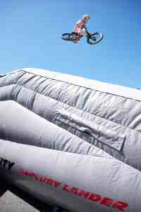 Young mountain biker in a red and white checkered kit executing a high jump over a Gravity Mercury Lander airbag
