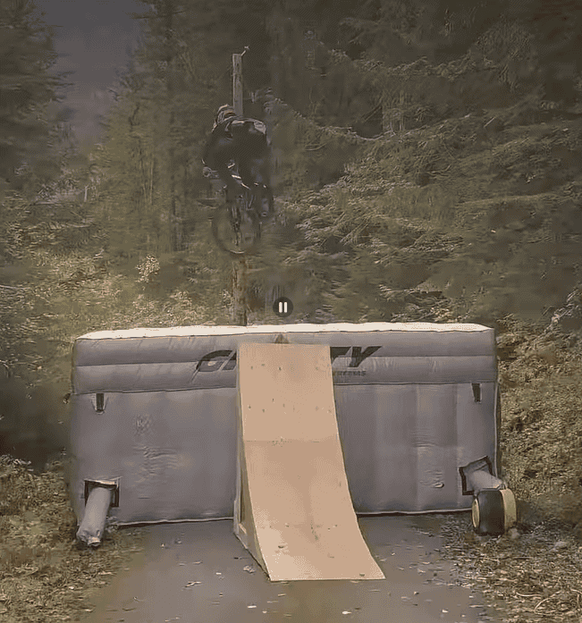 MTB rider in the forest, midflight from a wooden ramp onto a landing pad